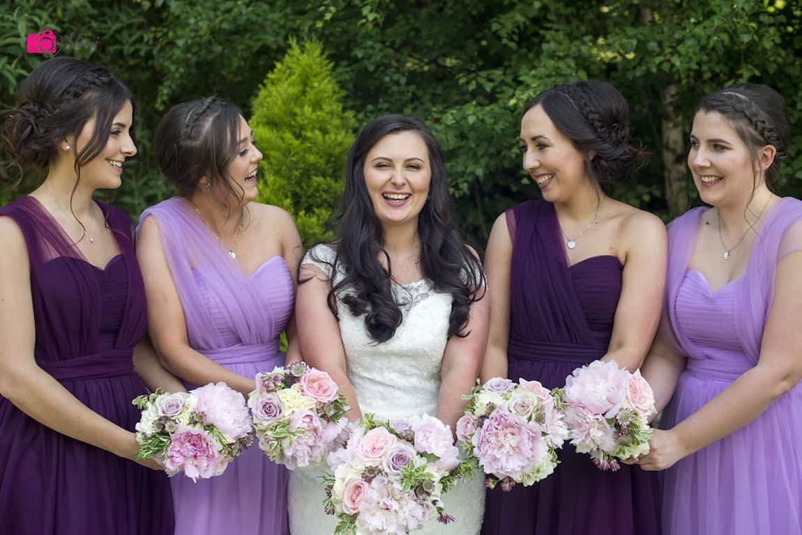 bride and bridesmaids laughing while taking picture in greenery