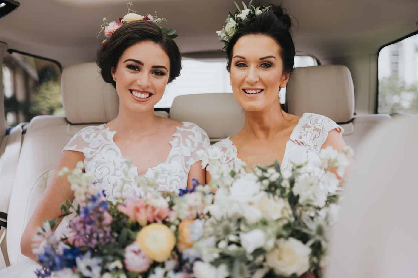 bride and bridesmaid holding bouquet of flowers inside a car