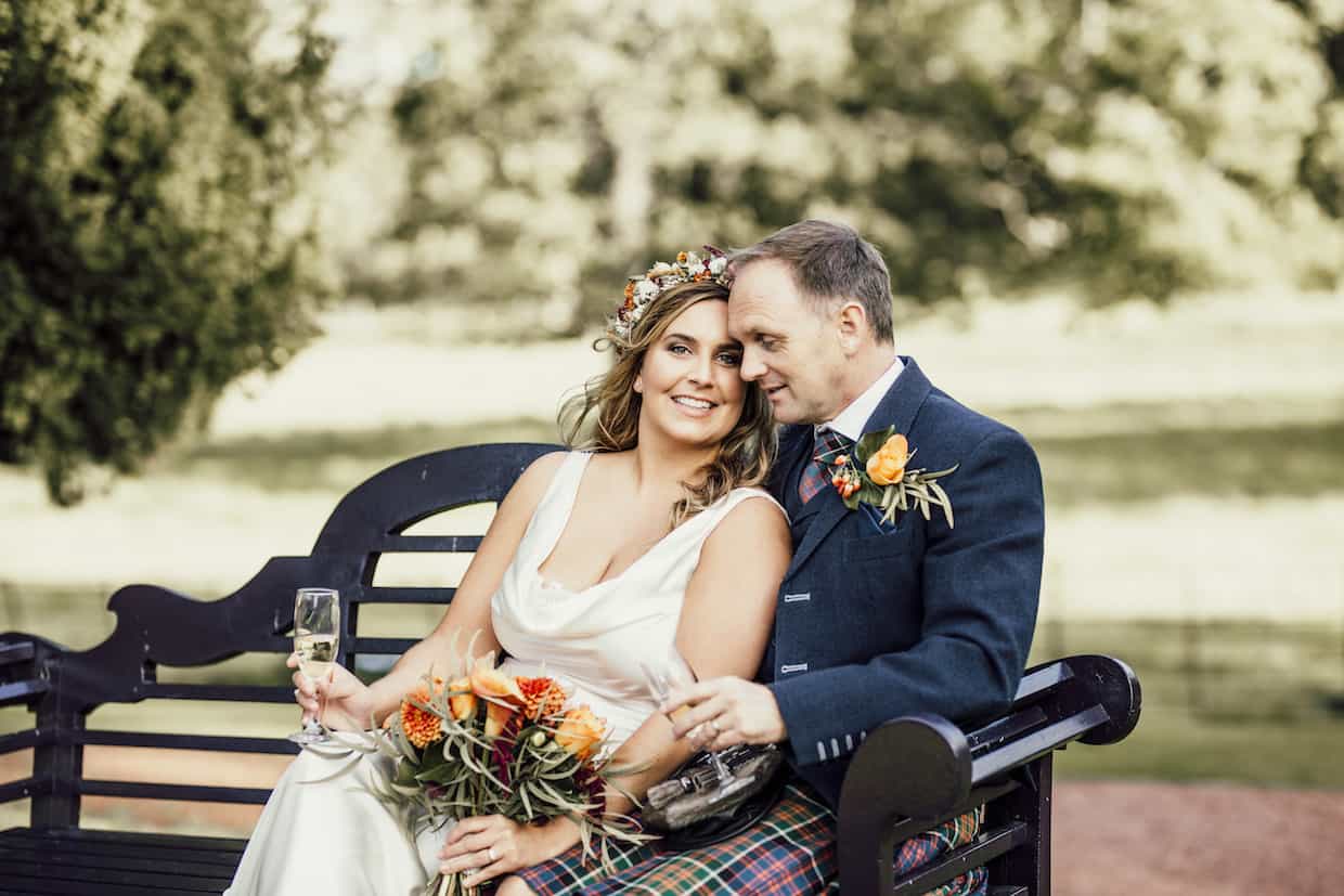 bride holding flowers and groom sitting on bench